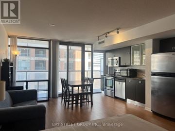 Toronto (Bay Street Corridor) condo for rent - A modern kitchen with a dining table and chairs in the foreground and a view of a cityscape through the windows.
