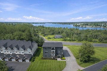 Gravenhurst apartment for rent - A large building with a grey roof is surrounded by a grassy area and a lake in the distance.