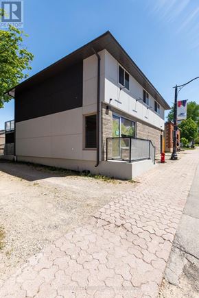 Arran-Elderslie apartment for rent - A modern building with a white and black facade is situated on a street with a paved sidewalk.
