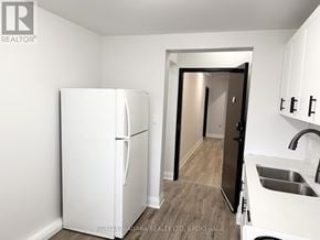 Niagara Falls (Downtown) multi-family for rent - A white refrigerator in a kitchen with a sink and a doorway leading to another room.