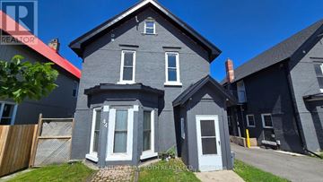 Orillia fourplex for rent - A grey house with a red roof is in front of a blue sky.