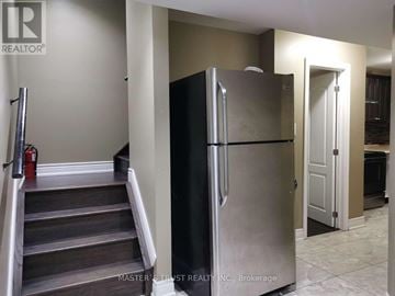 East Gwillimbury apartment for rent - A stainless steel refrigerator stands in a kitchen with a staircase to the left.