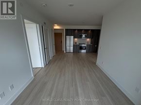 Toronto (Islington-City Centre West) condo for rent - A spacious room with wooden flooring and a kitchen area in the background.