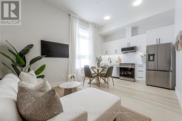 Barrie (Wellington) condo for rent - A modern living room with a white couch and a television mounted on the wall.