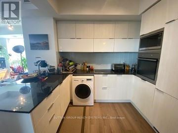 Toronto (Waterfront Communities) condo for rent - A modern kitchen with white cabinets and a black countertop.