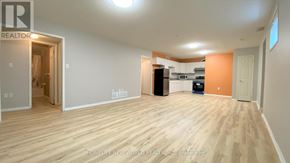Barrie (Georgian Drive) apartment for rent - A large empty room with wooden flooring and a kitchen area in the background.