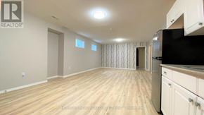 Barrie (Georgian Drive) apartment for rent - A spacious room with wooden flooring and a kitchen area with white cabinets.