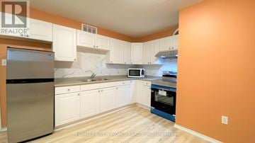 Barrie (Georgian Drive) apartment for rent - A kitchen with white cabinets and a stainless steel refrigerator.