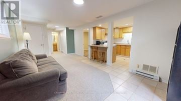Guelph (Kortright West) apartment for rent - A living room with a grey couch and a kitchen area in the background.