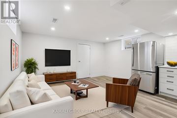 Hamilton (Parkview) apartment for rent - A modern living room with a white sofa, a wooden armchair, a coffee table, a flat-screen TV, and a kitchen area with a refrigerator and a bowl of bananas.