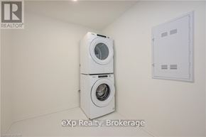 Centre Wellington (Elora/Salem) condo for rent - A white dryer and washer are stacked on top of each other in a small, white-walled laundry room.