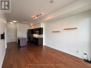 Toronto (Waterfront Communities) condo for rent - A spacious room with wooden floors and white walls, furnished with a kitchenette and a bar area.