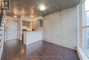 Toronto (Niagara) condo for rent - A spacious, empty room with a kitchen area in the background.