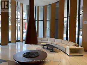 Toronto (Bay Street Corridor) condo for rent - A large room with a long white couch and a table in front of a glass wall.