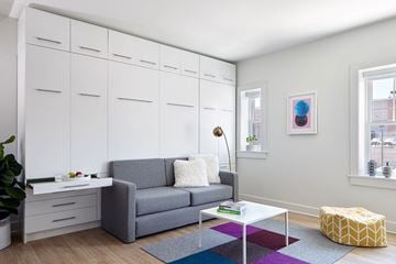 Omaha apartment for rent - A grey couch with a white pillow and a grey blanket sits in a living room with a white cabinet and a window.