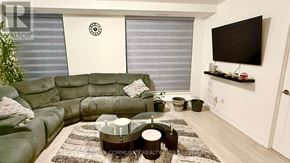 Oshawa (Windfields) condo for rent - A living room with a green sofa and a flat screen TV mounted on the wall.
