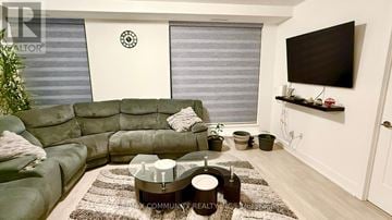 Oshawa (Windfields) condo for rent - A living room with a green sofa and a flat screen TV mounted on the wall.