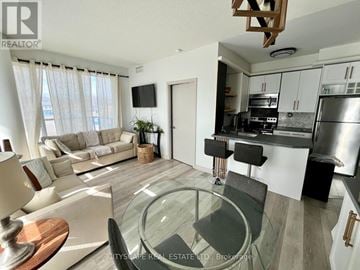 Toronto (Regent Park) condo for rent - A modern living room with a glass table and a kitchen area in the background.