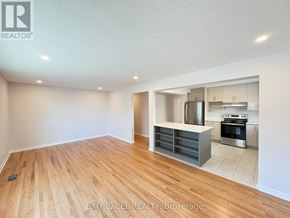 Ottawa multi-family for rent - A spacious room with wooden flooring and a kitchen area in the background.