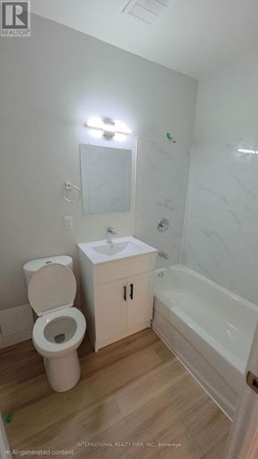Hamilton (Mcquesten) multi-family for rent - A white toilet sits next to a sink in a small bathroom.