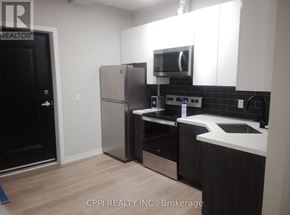 Peterborough (Town Ward 3) condo for rent - A kitchen with a black door, a refrigerator, a microwave, and a counter.