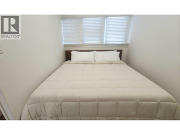 Vancouver apartment for rent - A bed with a white comforter and two pillows in a room with a window.