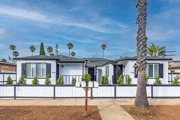 Carlsbad apartment for rent - A white house with a black fence and a palm tree in front.