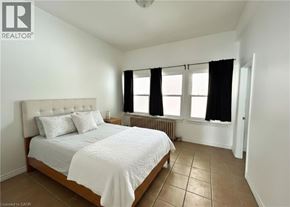 Hamilton apartment for rent - A bedroom with a bed, two pillows, a radiator, and a window with black curtains.