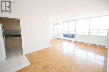Toronto (Playter Estates-Danforth) condo for rent - A room with a wooden floor and white walls, with a kitchen area to the left.