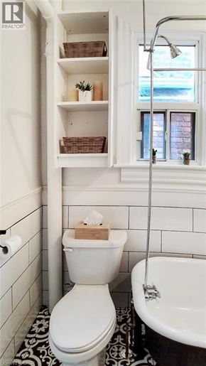 Hamilton apartment for rent - A white toilet with a wooden toilet paper holder sits in a bathroom with a white tub and a window.