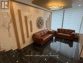 Toronto (Flemingdon Park) condo for rent - A living room with a brown leather couch and a clock on the wall.