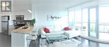 Toronto (Mimico) condo for rent - A living room with a couch and a kitchen area in the background.