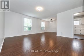 Guelph (Victoria North) apartment for rent - A spacious room with wooden flooring and white walls, with a window and a kitchen area visible in the background.