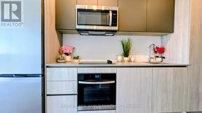Toronto (Newtonbrook West) condo for rent - A modern kitchen with a refrigerator, microwave, oven, and a countertop with flowers.
