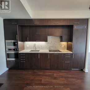 Toronto (Willowdale East) condo for rent - A kitchen with dark wood cabinets and a marble backsplash.