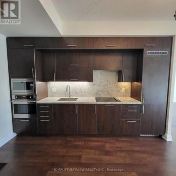 Toronto (Willowdale East) condo for rent - A kitchen with dark wood cabinets and a marble backsplash.