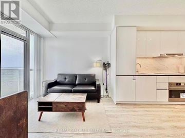 Vaughan (Vaughan Corporate Centre) condo for rent - A living room with a black leather sofa and a wooden coffee table.