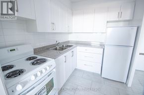 Toronto (East York) condo for rent - A white kitchen with a stove, sink, and refrigerator.