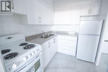 Toronto (East York) condo for rent - A white kitchen with a stove, sink, and refrigerator.