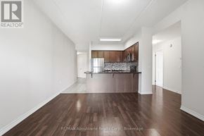 Guelph (Kortright West) condo for rent - A spacious room with wooden floors and a kitchen area in the background.