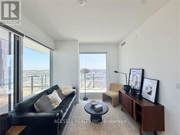 Vaughan (Vaughan Corporate Centre) condo for rent - A living room with a black couch and a large window overlooking a cityscape.