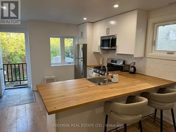 Toronto (Lawrence Park North) townhouse for rent - A kitchen with a wooden table and chairs, and a window with a view of trees.