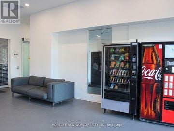 Oshawa (Samac) condo for rent - A modern living room with a grey couch and a Coca-Cola vending machine.