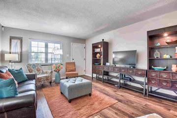 Topeka apartment for rent - A living room with a brown leather couch, a grey ottoman, a wooden floor, and a television on a stand.
