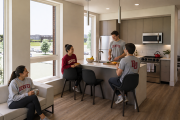 Denver apartment for rent - A man in a grey shirt is cooking in a modern kitchen with two women sitting at a table.