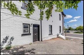 Orillia apartment for rent - A white building with a black door and windows is surrounded by trees.