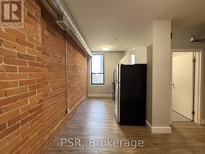 Toronto (Junction Area) condo for rent - A hallway with a brick wall on the left and a black refrigerator on the right.