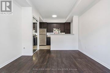 Brampton (Sandringham-Wellington) townhouse for rent - A spacious room with wooden floors and white walls, featuring a kitchen area with dark brown cabinets and a refrigerator.