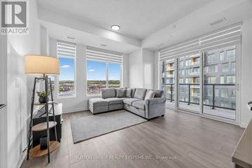 Burlington (Alton) condo for rent - A well-lit living room with a grey sofa and a large window.
