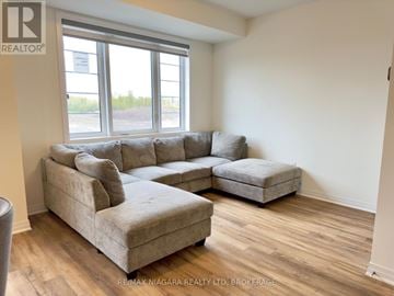 Welland (Dain City) townhouse for rent - A living room with a grey couch and a smaller couch in front of a window.